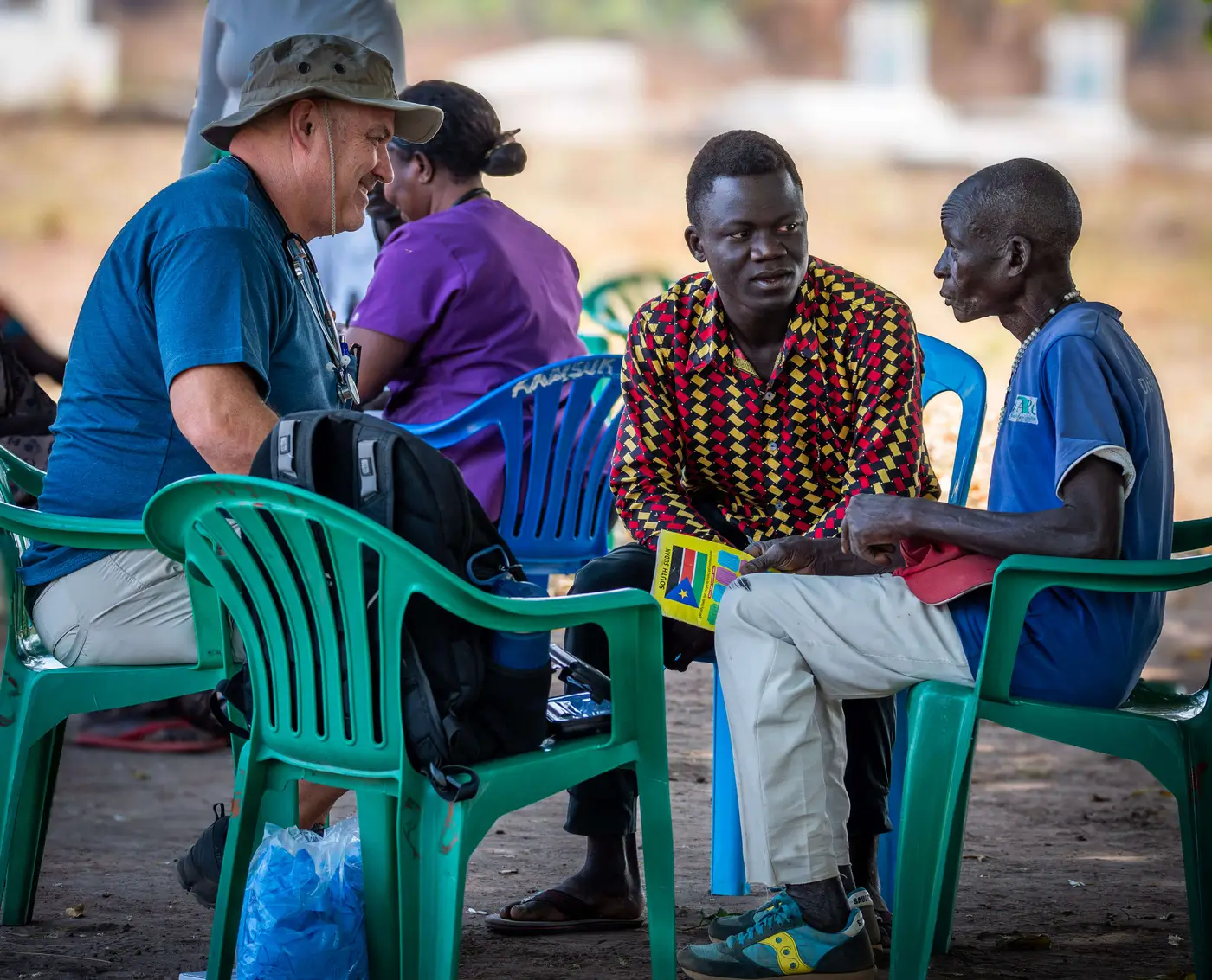 A healing Kadi doctor sitting with a group of Sudanese people chatting.