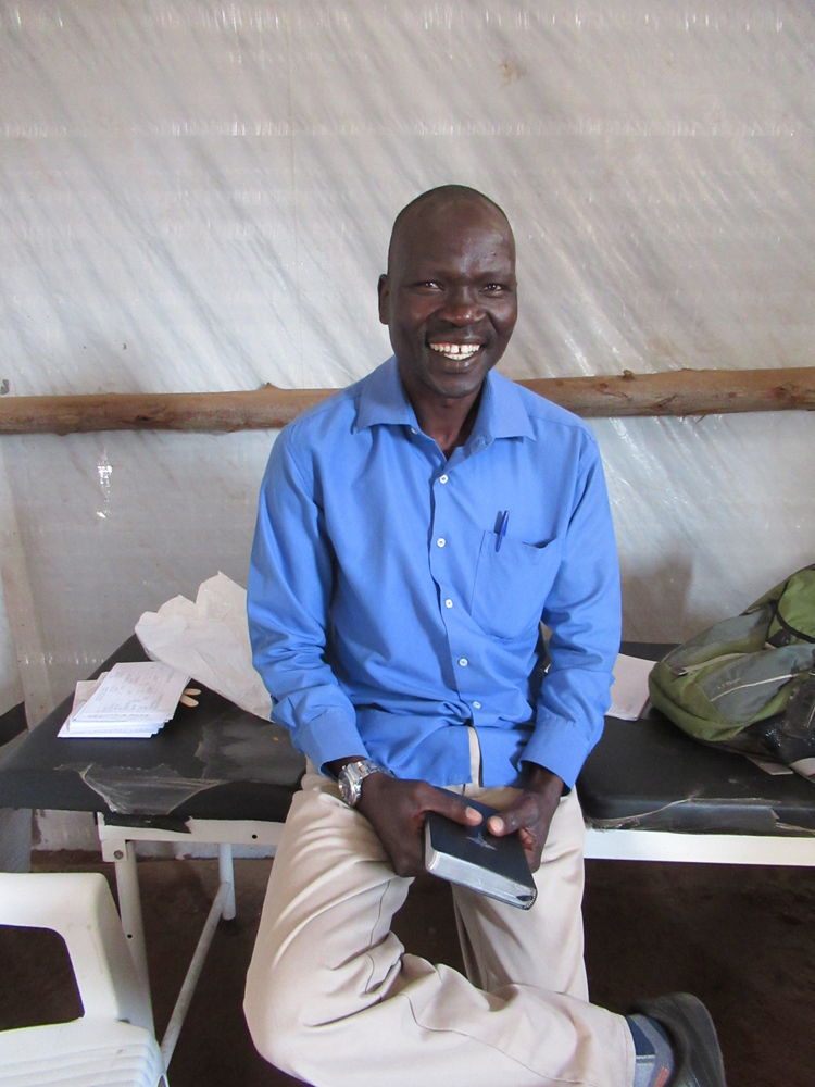 A young sudanese man smiling, laughing and holding a Bible.